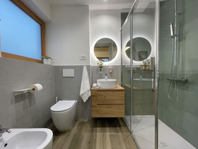 Bagno con doccia in vetro, lavabo e specchio tondo