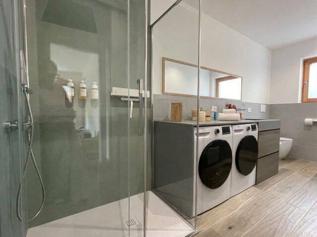 Bagno con doccia in vetro, lavatrice e asciugatrice