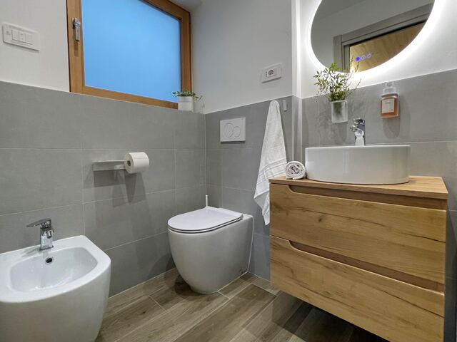 Bagno privato con mobile in legno, specchio tondo retroilluminato e doccia in vetro