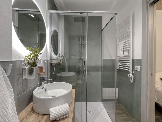 Bagno con lavabo su mobile in legno, specchio tondo e termoarredo