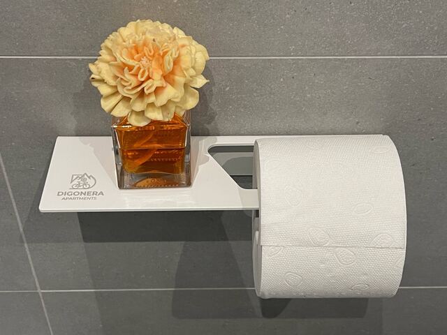 Dettaglio del bagno con fiore e portarotolo con il logo Digonera