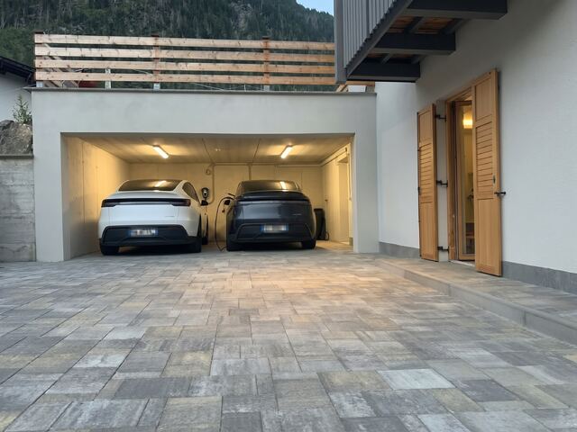 Il garage coperto di Digonera con due auto elettriche, una in ricarica alla wallbox, e il cortile pavimentato
